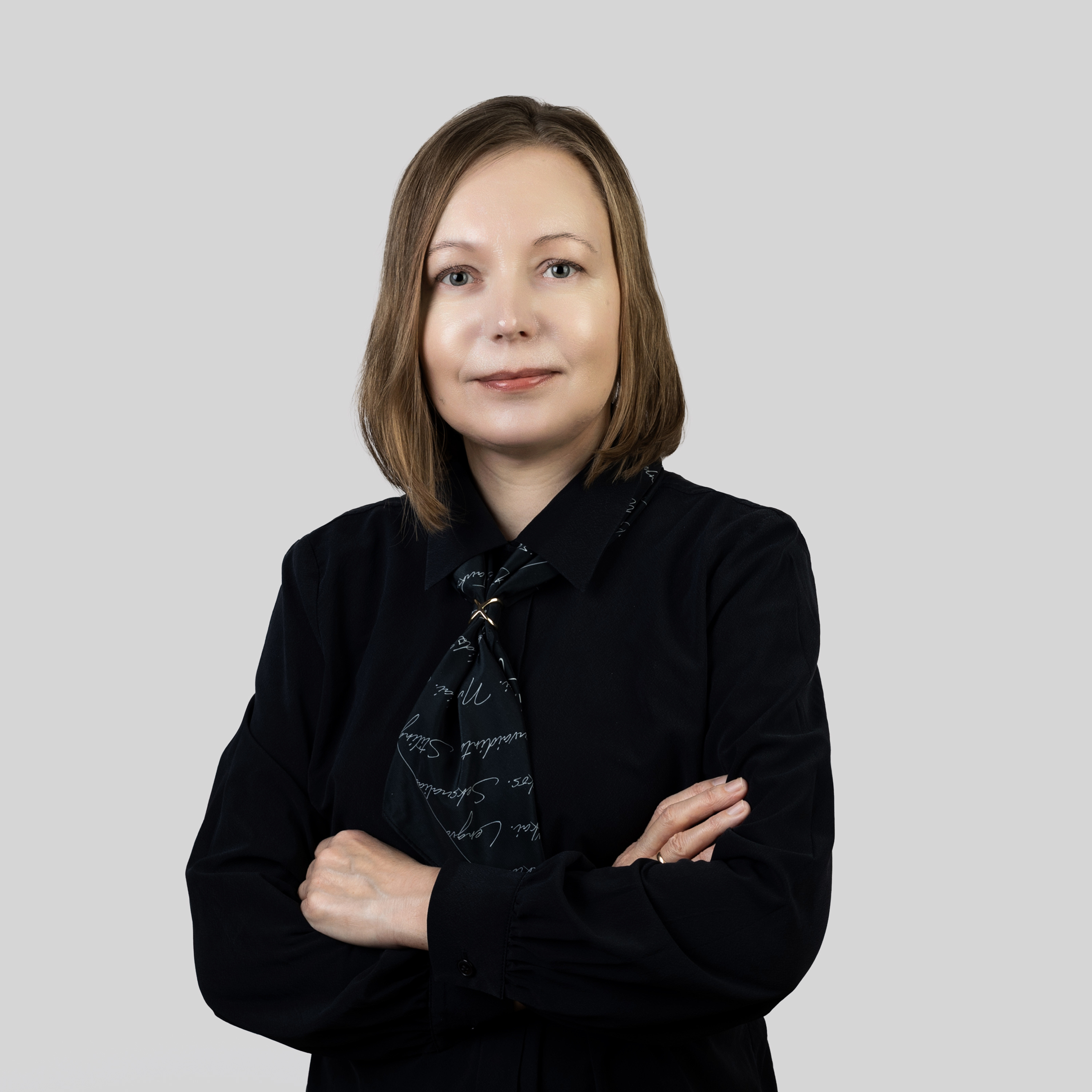 Šarūnė Kriaučiūnienė | KTU Centre for Teacher Education “iSTEAM” Portrait of a woman with shoulder-length light brown hair, wearing a black blouse and jacket, standing with her arms crossed against a light grey background.